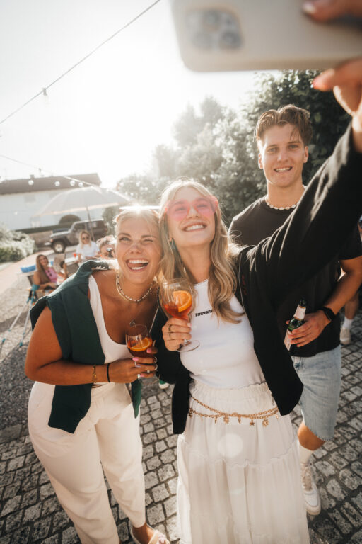 Junge Freundesgruppe beim Selfie, lachend mit Aperol Spritz und Strawanza-Outfits, Sommerparty-Vibes.