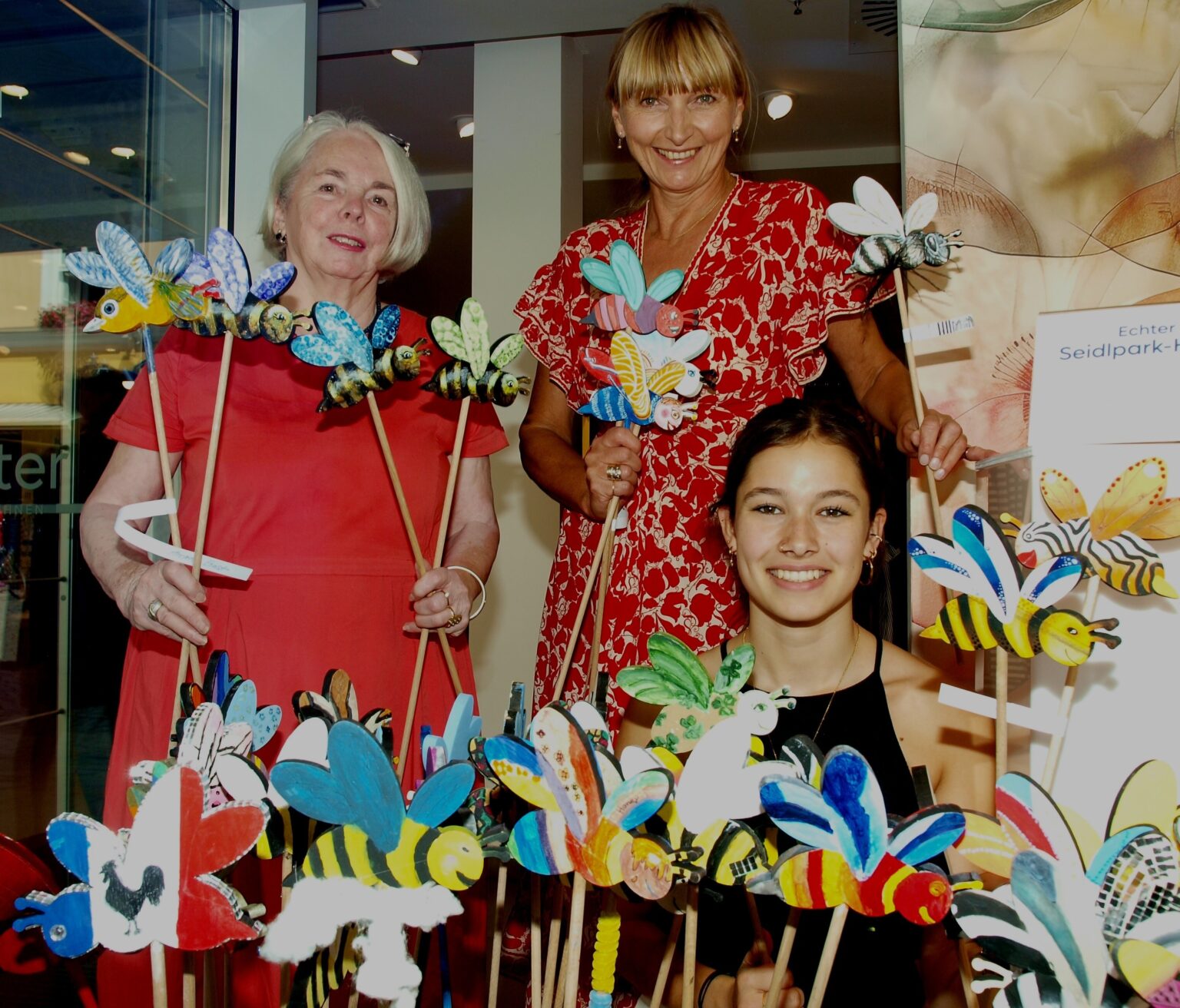 Förderkreis Parklandschaft: Bemalte Holzbieren bei Echter. Heidi Wieland von Seidlpark und Milena Misera und Tabea Adelwarth von Echter Mode in Murnau sind vor dem Schaufenster mit den buntbemalten Bienen