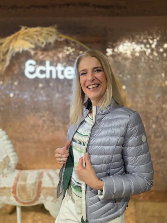 Eine Modeberaterin zeigt ihre graue Damenjacke als Frühjahrslook vor der Shimmerwall bei Echter Mode in Weilheim