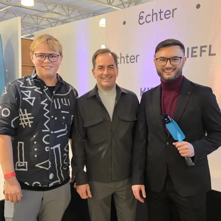 Geschäftsführer von Kiefer, Echter Mode und der Moderator stehen vor einer Echter-Kiefl-Fotowand im Kiefl Gartencenter in Gauting und lächeln in die Kamera.