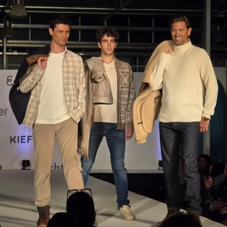 Drei Männer präsentieren helle Cordhosen, Strickpullover und Jacken in Naturtönen auf der Kiefl-Bühne im Gartencenter bei der Großen Echter Modenschau.