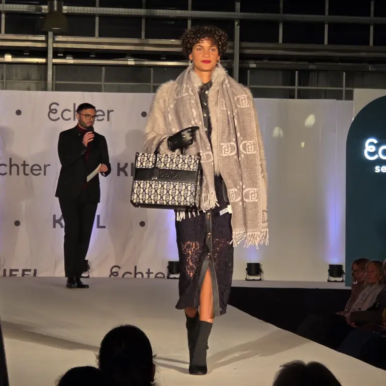 Model trägt dunkelblauen Rock, Strickjacke und große graue Schal mit Tasche auf der Kiefl-Bühne bei der Großen Echter Modenschau.