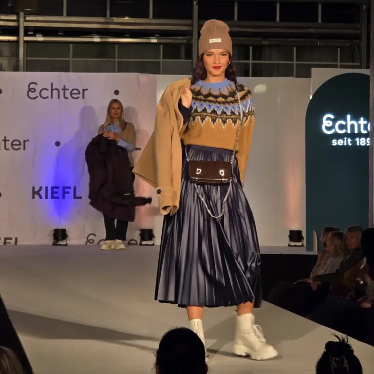 Model mit braunem Strickpullover, Faltenrock und Beanie auf dem Laufsteg auf der Kiefl-Bühne im Gartencenter in Gauting bei der Großen Echter Modenschau