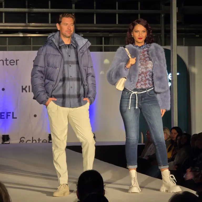 Mann und Frau tragen winterliche Outfits in Blautönen mit Steppjacke und Fake-Fur-Jacke auf der Kiefl-Bühne im Gartencenter in Gauting bei der Großen Echter Modenschau