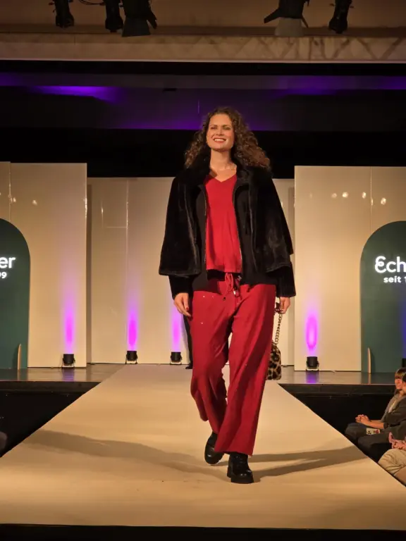 Model in rotem Hosenanzug und dunkler Jacke auf dem Laufsteg bei Echter Mode in Murnau