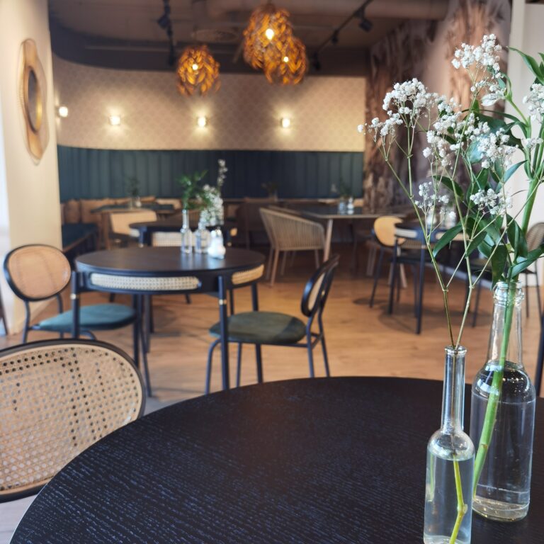 Stillvolles Café CouCou im Echter Modehaus mit Holzmöbel und schönen Lampen mit warmen Licht. Auf den Tischen stehen kleine Blumensträuße