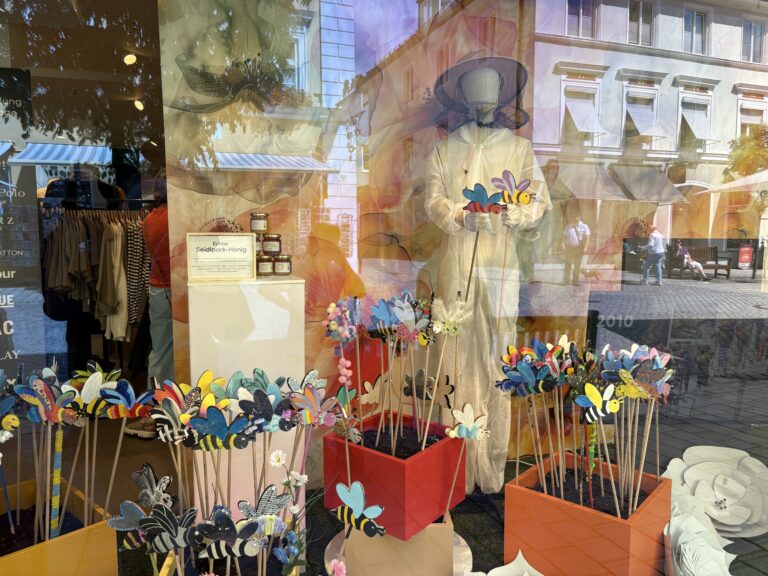 Schaufenster von Modehaus Echter mit bunt bemalten Holzbienen auf Stäben, einer Schaufensterpuppe im Imkeranzug und einem Infostand zur Benefizaktion für den Seidlpark Murnau.