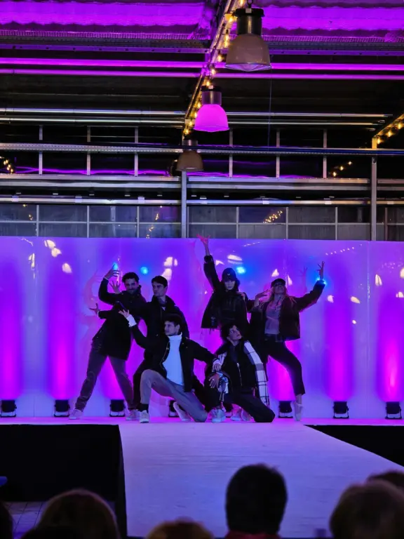 Tanzgruppe in gemeinsamer Pose vor einer violett und blau beleuchteten Bühnenwand.