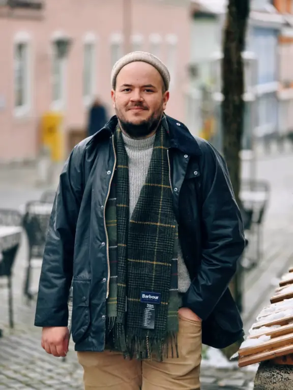 Laurenz aus Starnberg trägt eine klassische Barbour-Jacke, grauen Strick und karierten Winterschal auch von Barbour..