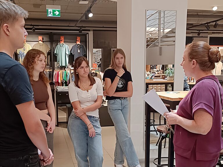 Neue Azubis stehen im Modehaus Echter und hören der Hausleitung aufmerksam zu