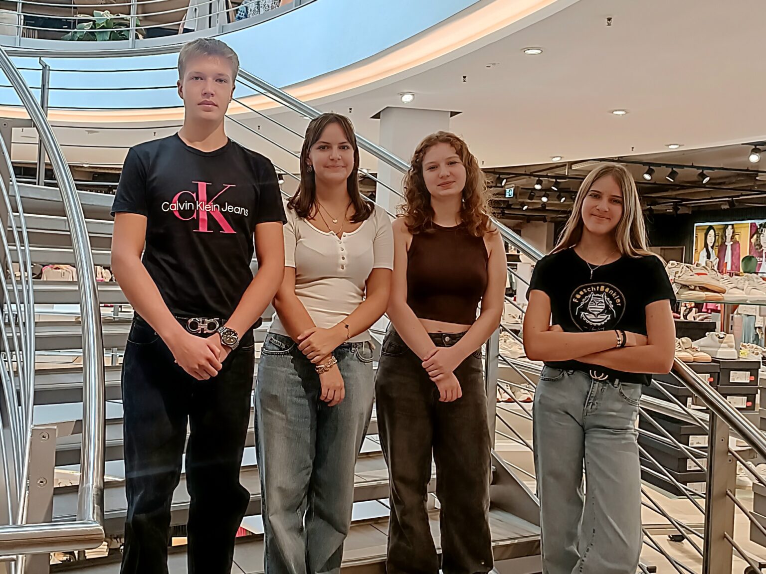 Vier neue Auszubildende stehen auf der Treppe im Modehaus Echter in Weilheim und blicken freundlich in die Kamera.