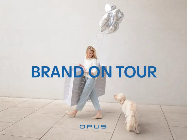 OPUS Brand on Tour Motiv mit Frau, OPUS Einkaufstaschen, silbernen Ballons und Hund.