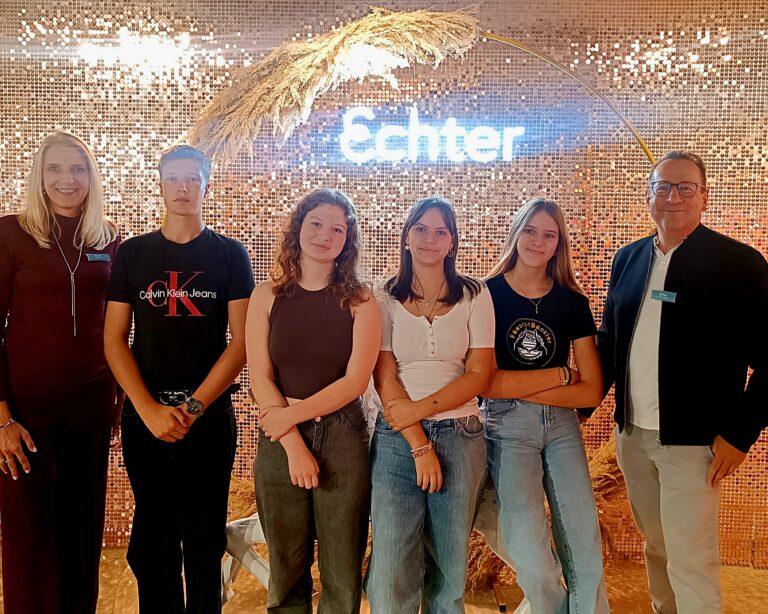 Fröhliche Azubis, der stellvertretender Geschäftsführer und die Personalleiterin schauen freudig in die Kamera bei Echter Schimmerwand.