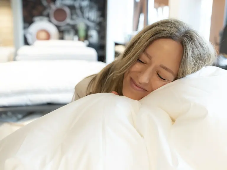 Frau liegt lächelnd auf einem weichen, weißen Bettwaren-Kissen in der Schlafabteilung von Echter Wohnen.