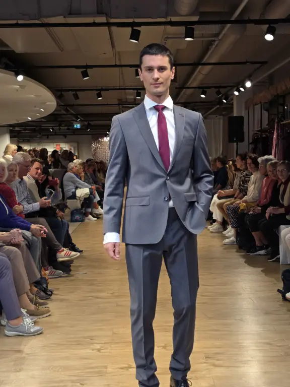 Model im grauen Anzug und roter Krawatte auf dem Laufsteg bei der Großen Echter Modenschau in Weilheim am 27.09.2025