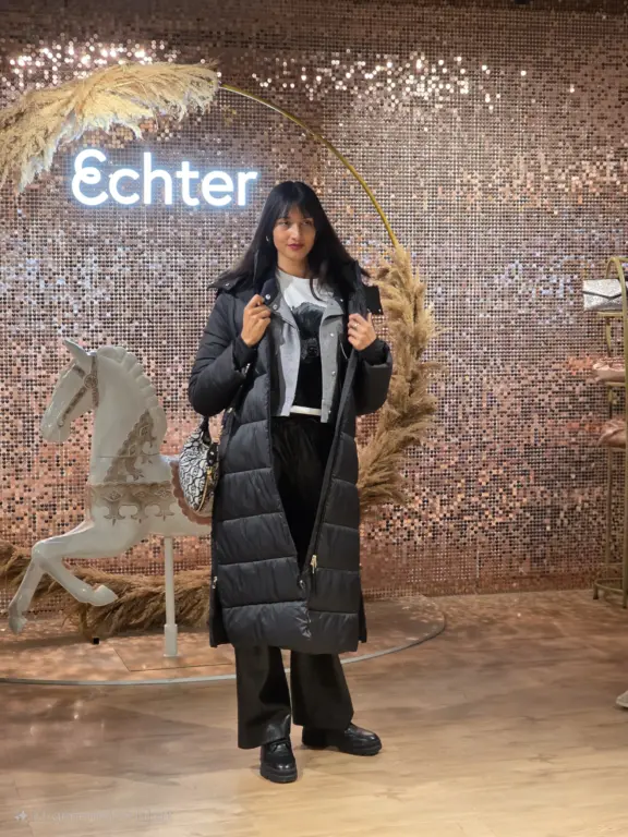 Model im schwarzen Daunenmantel mit Lederhose vor der Echter-Schimmerwand bei der Großen Modenschau in Weilheim am 27.09.2025